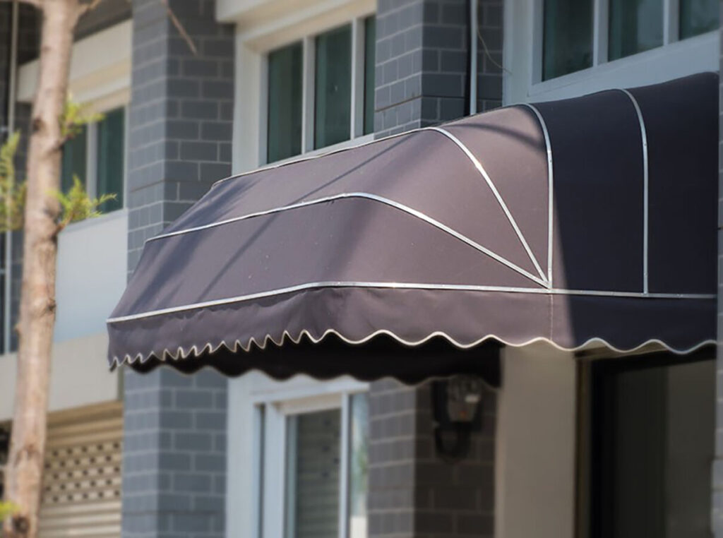 Modern bir binanın kapısının üzerinde kurulu, koyu renkli, "karpuz dilimi" olarak da bilinen körüklü tente modeli.