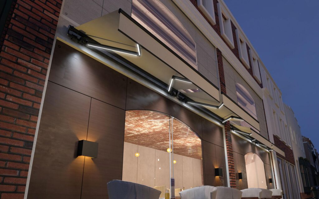 Modern bir kafe cephesinde, üzerinde entegre LED aydınlatmalar bulunan, açılmış halde duran mafsallı (kollu) tente sistemleri.