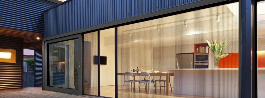 Modern bir verandaya açılan geniş sürgülü cam kapı üzerinde kurulu plise (pileli) sineklik sistemi.